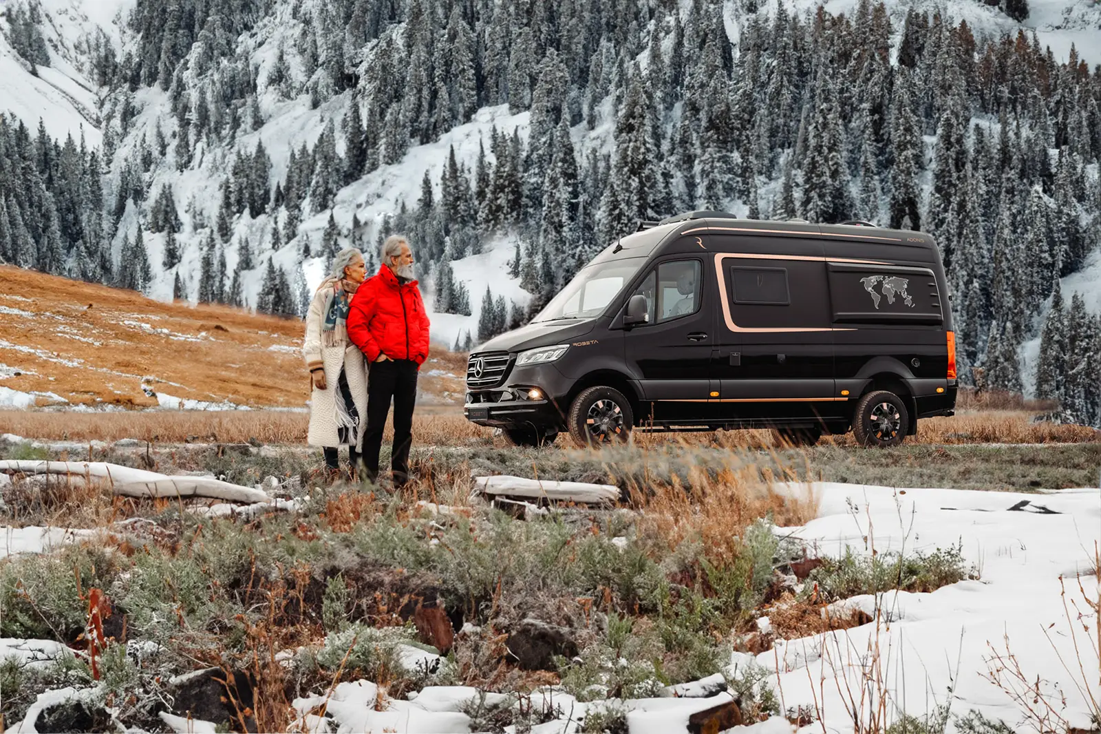 An elderly couple standing together in a snowy mountain landscape next to a black camper van.