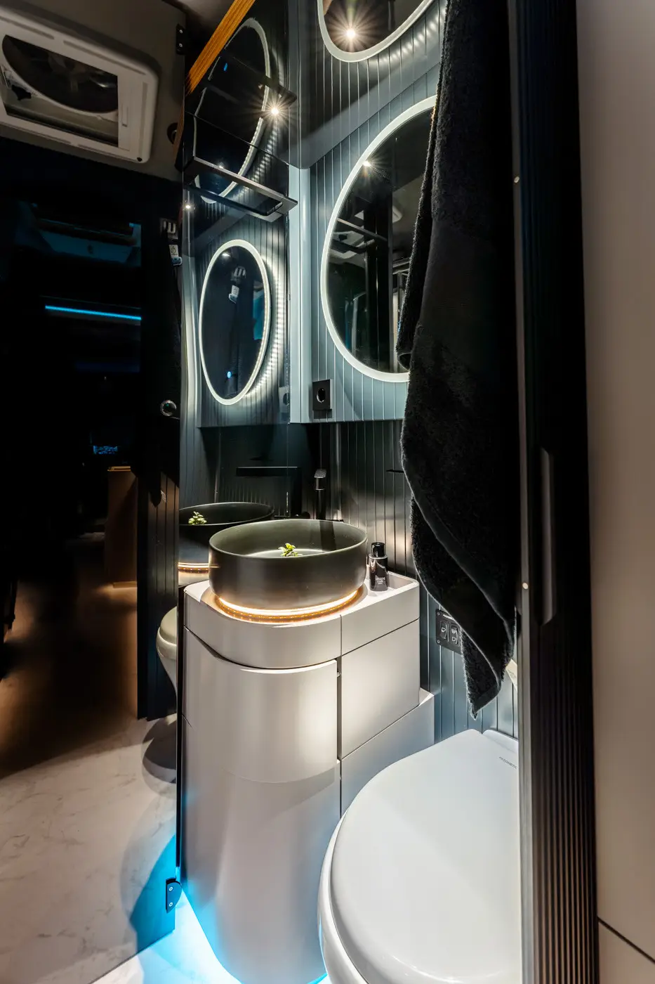 Interno di un bagno moderno con specchio rotondo illuminato, lavabo nero su un mobile bianco e toilette bianca.
