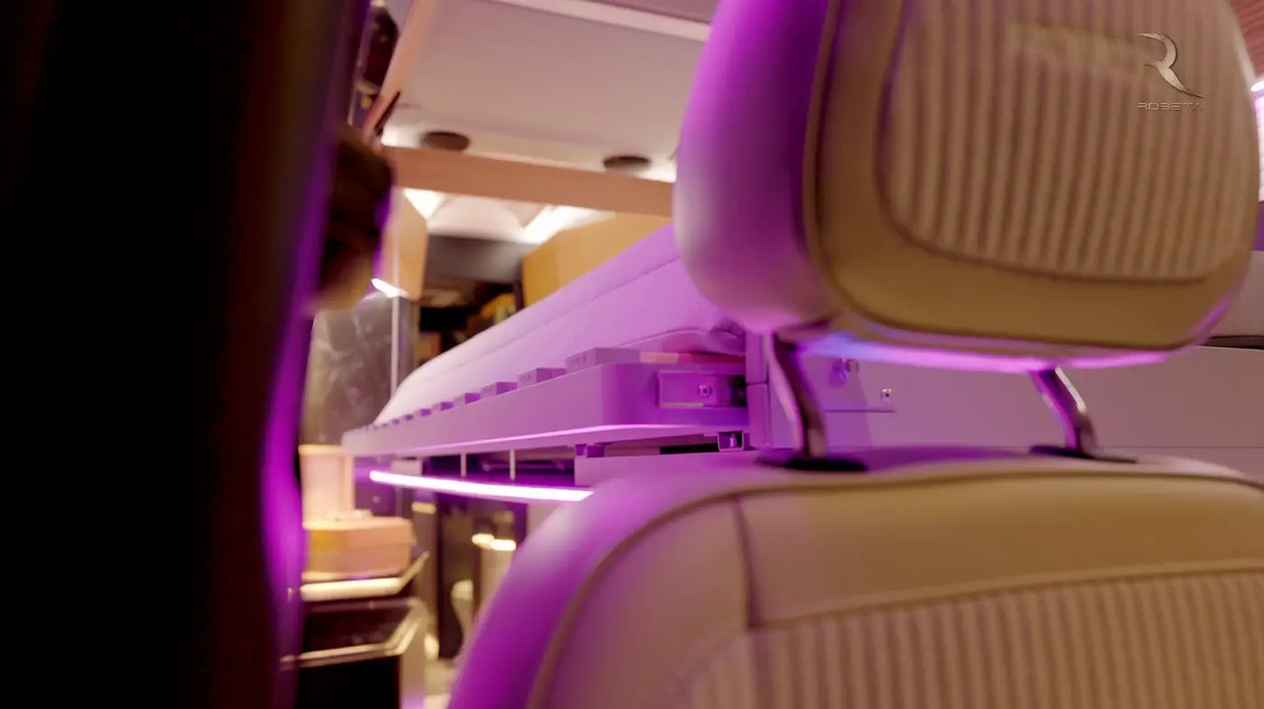 Vista interna di un veicolo che mostra un letto pieghevole con luci LED viola e poggiatesta in pelle beige.